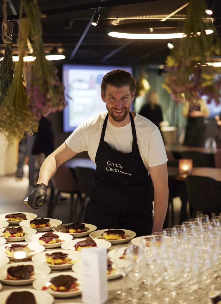 En man i förkläde serverar tallrikar med desserter i en restaurangmiljö.