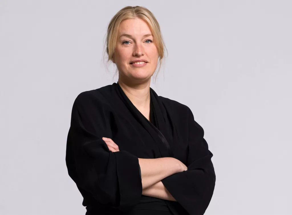 3. En person i mörka kläder står med armarna korsade mot en ljus bakgrund.