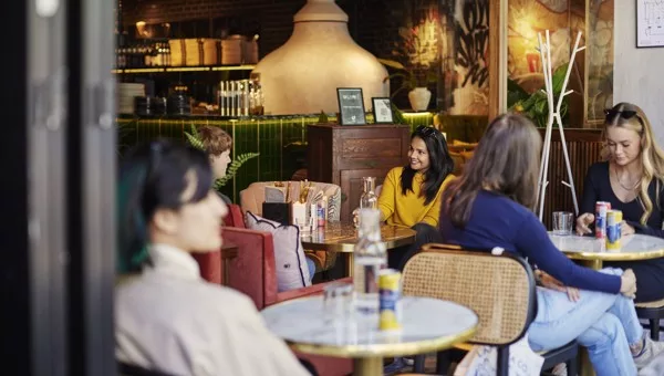 En grupp människor sitter vid runda bord och pratar i en stilfullt inredd restaurang med växter och dekorativa element.