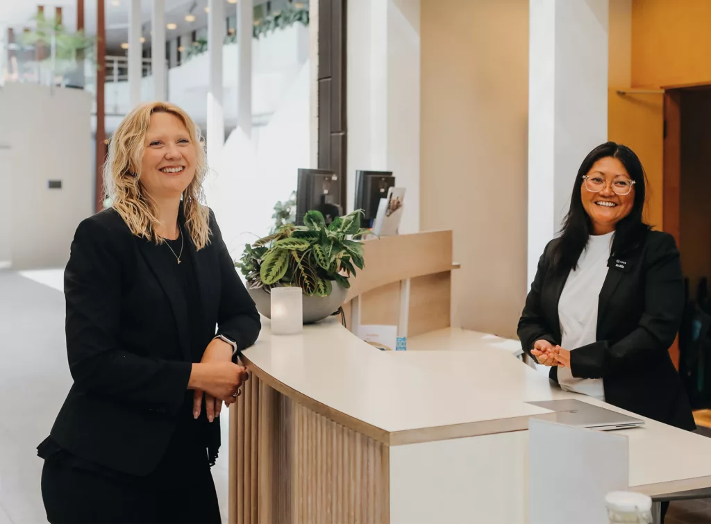 5. Två kvinnor står leende vid en receptionsdisk i ett modernt kontorsutrymme.