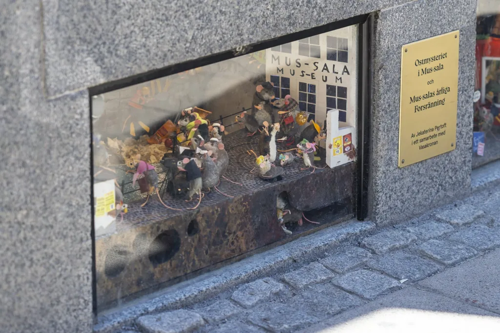 Ett miniatyrlandskap med små figurer bakom ett glas i en trottoar.