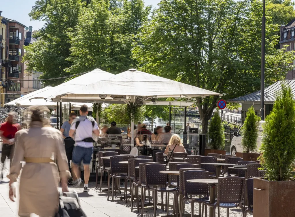 En uteservering med parasoller och stolar, omgiven av träd och människor.
