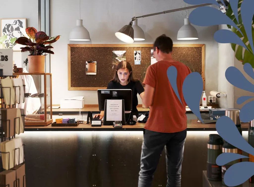 En person i orange tröja står vid en receptionsdisk och pratar med en anställd bakom disken.