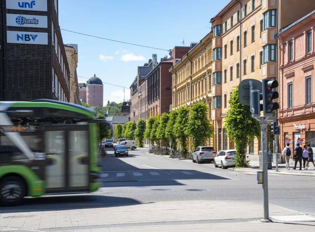 En grön spårvagn passerar längs en gata med färgglada byggnader och träd.