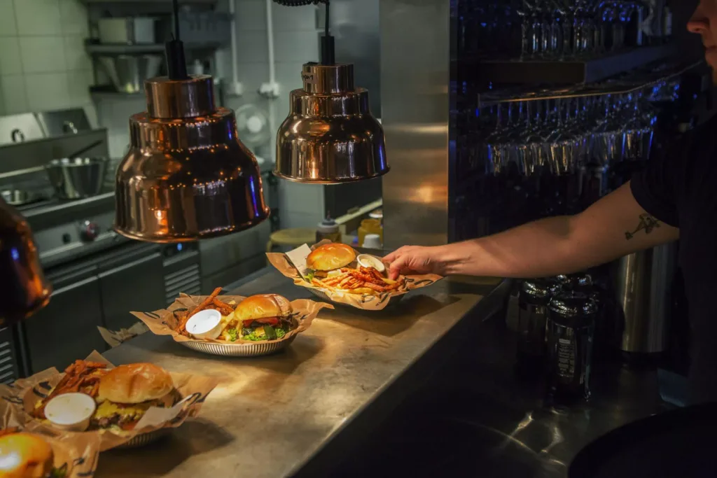 Hamburgare och pommes frites serveras på en disk under kopparlampor, medan en hand sträcker sig fram.