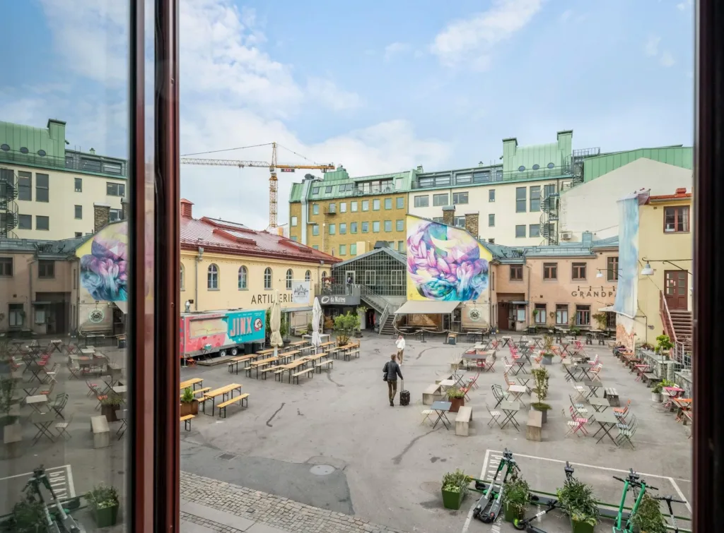En öppen innergård med uteserveringar, färgglada väggmålningar och byggnader i bakgrunden.