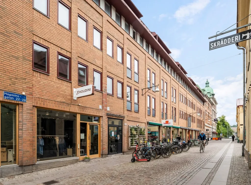 En gata kantad av tegelbyggnader, cyklar och butiker under en klar himmel.