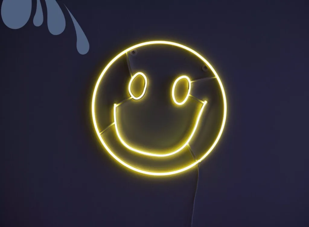 En gul neonfigur av en glad smiley på en mörk vägg.