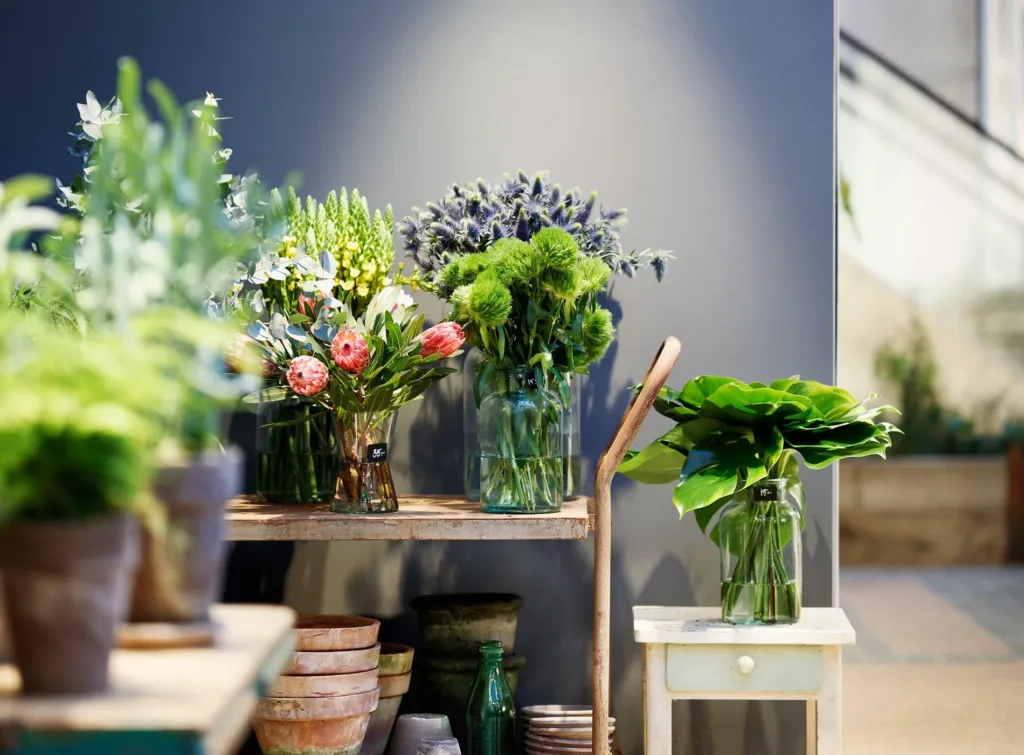 Dekorativ hylla med glasvaser fyllda med olika färska blommor och växter, omgiven av krukor.