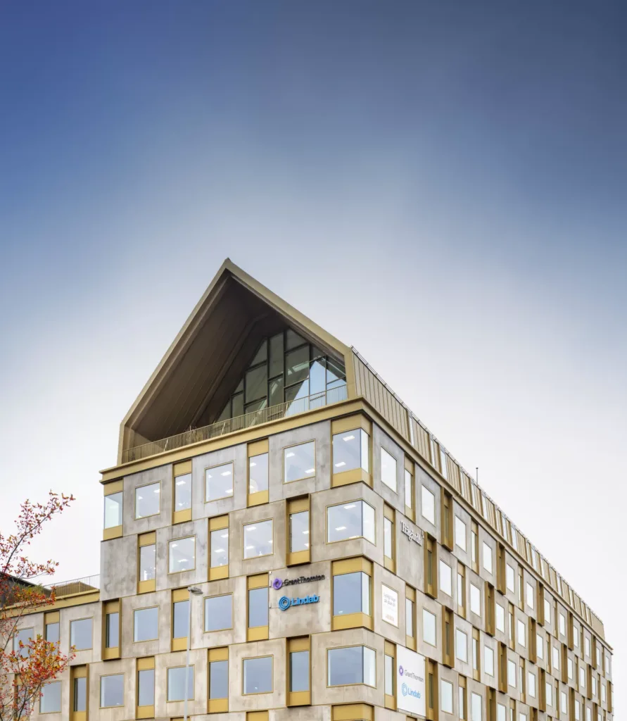 Byggnad med triangulärt tak och moderna fönsterfasader under en klar himmel.