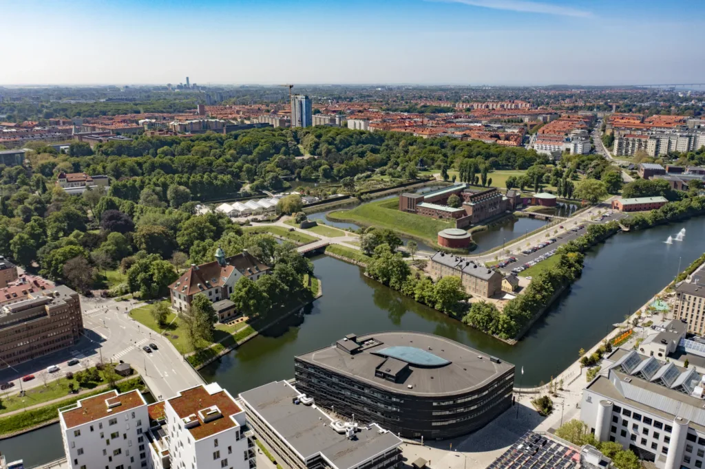En stadsvy med en park, kanal och moderna byggnader, sett från ovan.