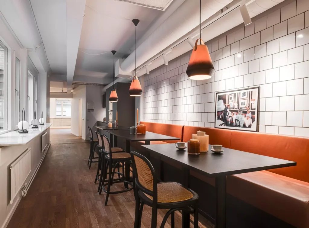 1. En modern restaurang med höga bord, stolar och hängande lampor med orange skärmar, samt tegelväggar och en inramad bild på väggen.