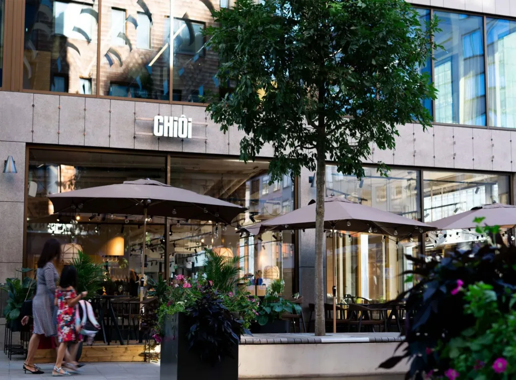 Restaurang med uteservering, parasoller och gröna växter, med texten "Chou" på fasaden.