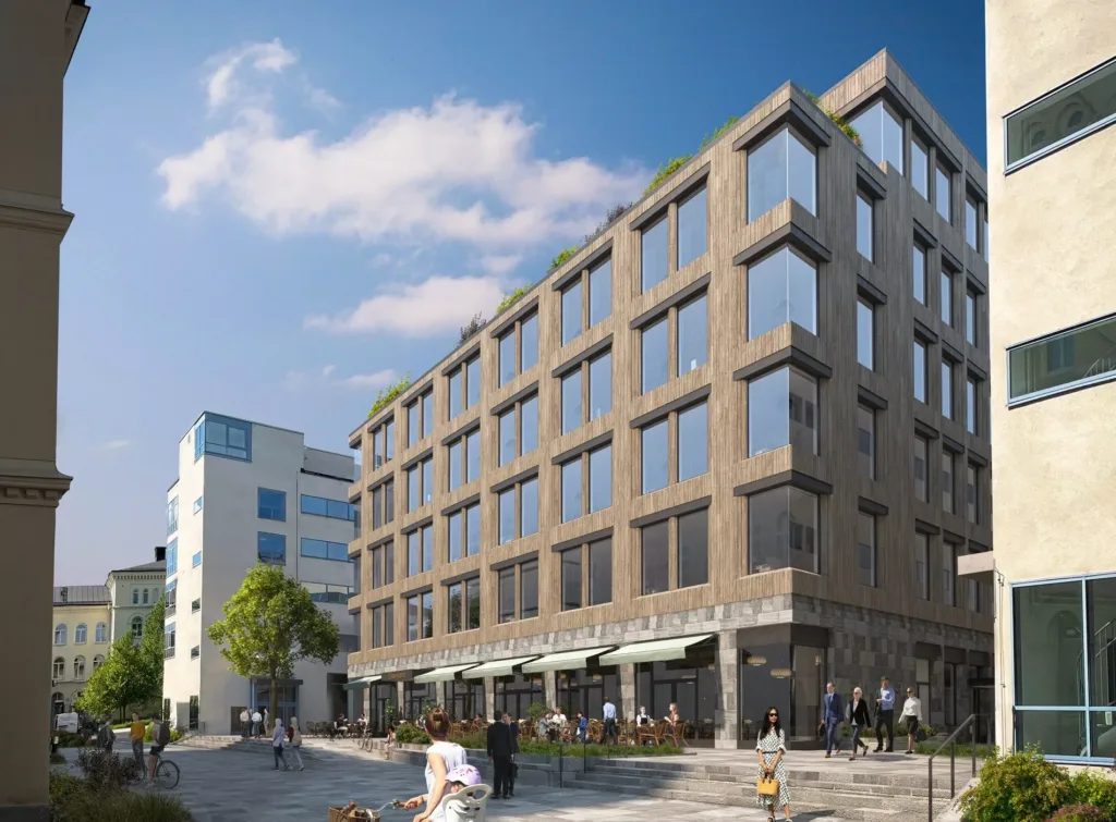 Modern byggnad med stora fönster, grön takväxt och en livlig trottoar med fotgängare.