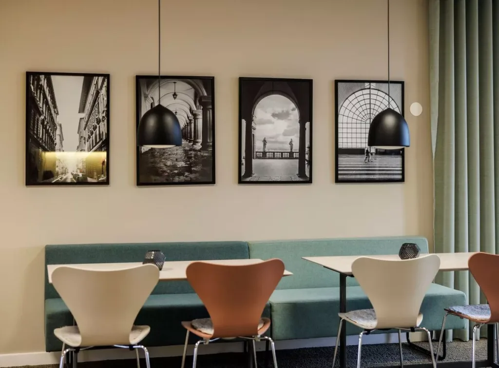En interiör med stolar och bord framför en vägg med svartvita fotografier som föreställer arkitektoniska motiv.