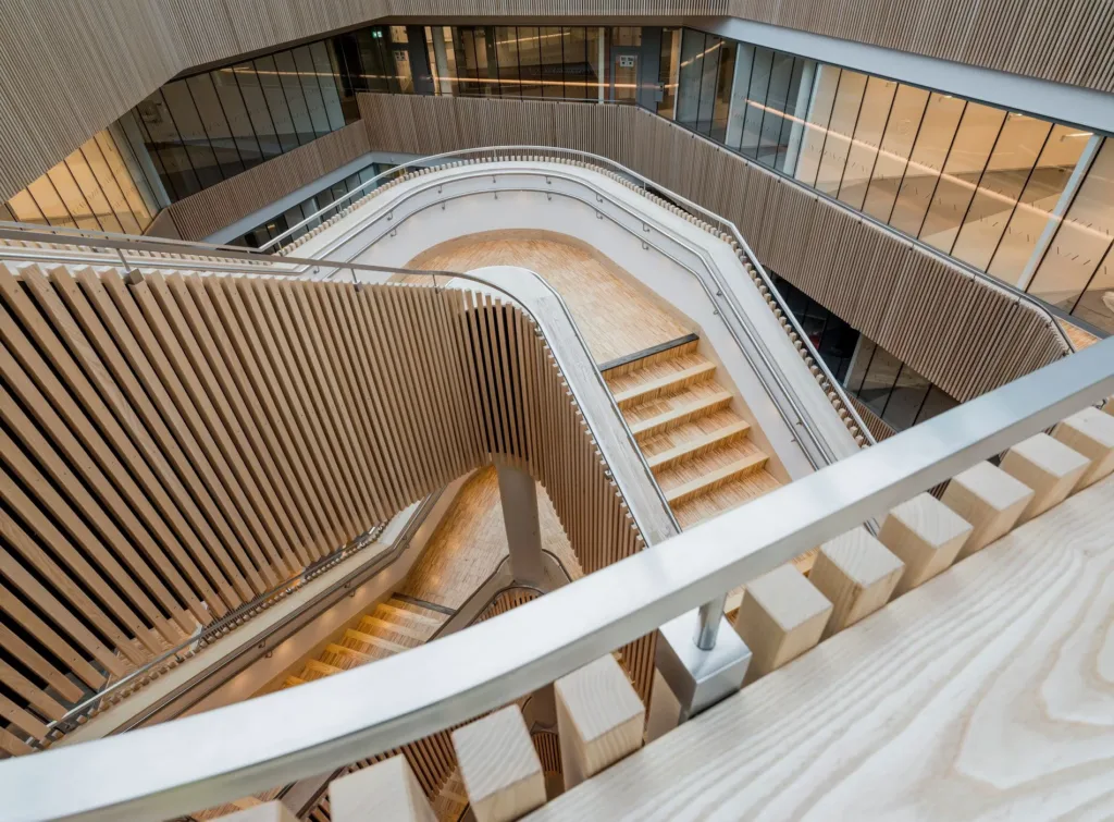 En spiraltrappa med trästeg och glasräcken i en arkitektoniskt modern byggnad.
