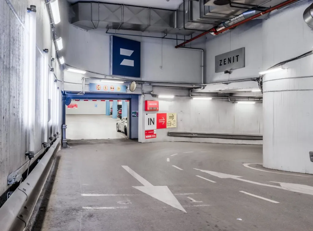 En parkeringsgarage med vita väggar, pilar på golvet som visar riktning och skyltar för in- och utgång.