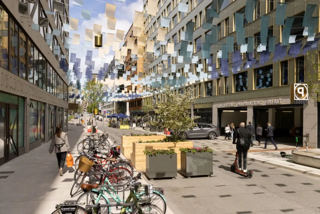 En stadsgata med cykelställ, planteringslådor och färgglada dekorationer hängande mellan byggnader.
