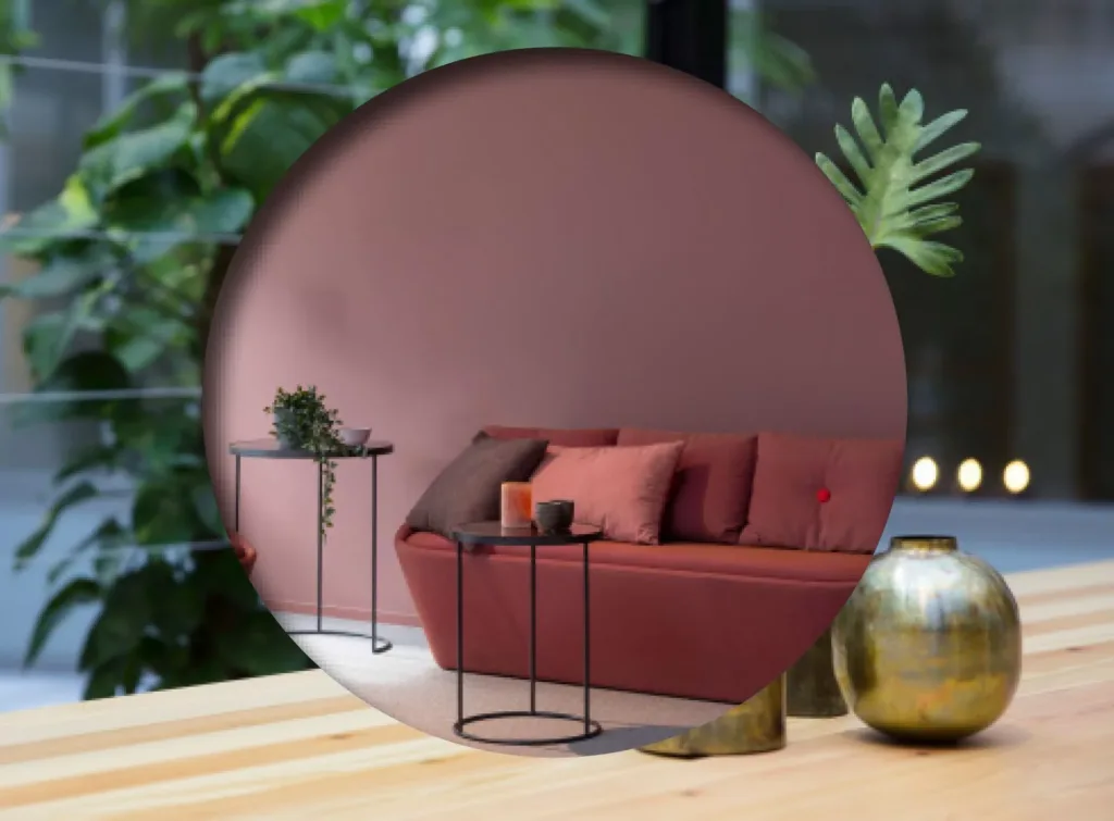 En rosa soffa med kuddar och små bord, reflekterad i en rund spegel.