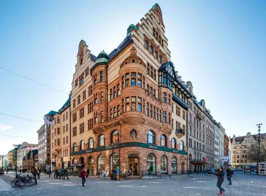 En hörnbyggnad med gotisk arkitektur, röda tegelväggar och gröna takdetaljer.