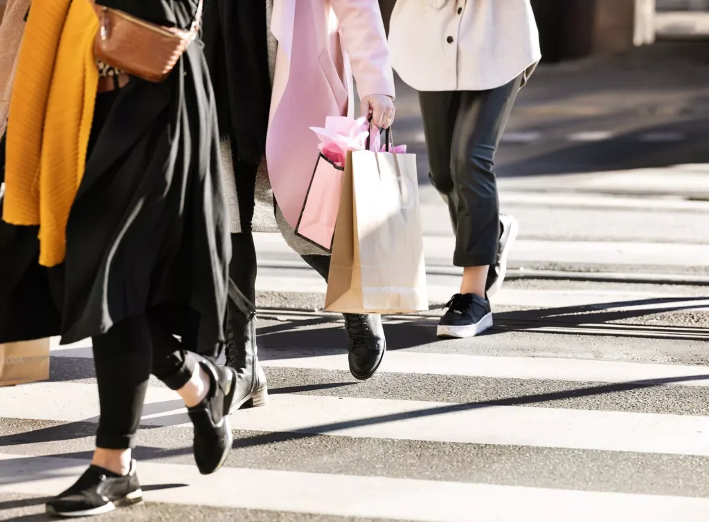 Flera personer går över ett övergångsställe, några bär shoppingkassar.