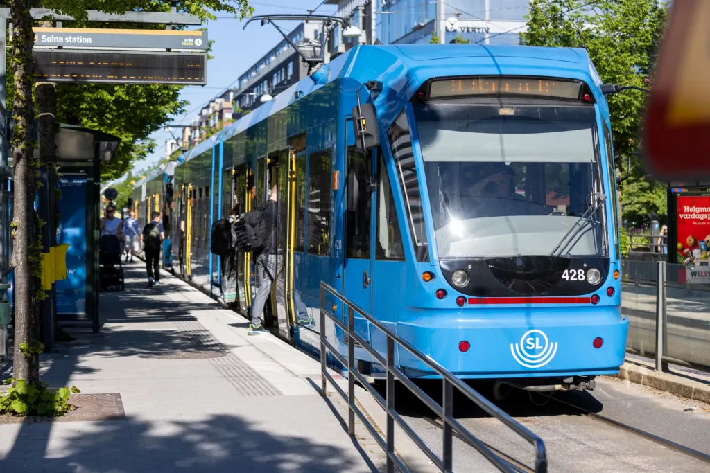 En blå spårvagn på en hållplats med människor som går på och av.