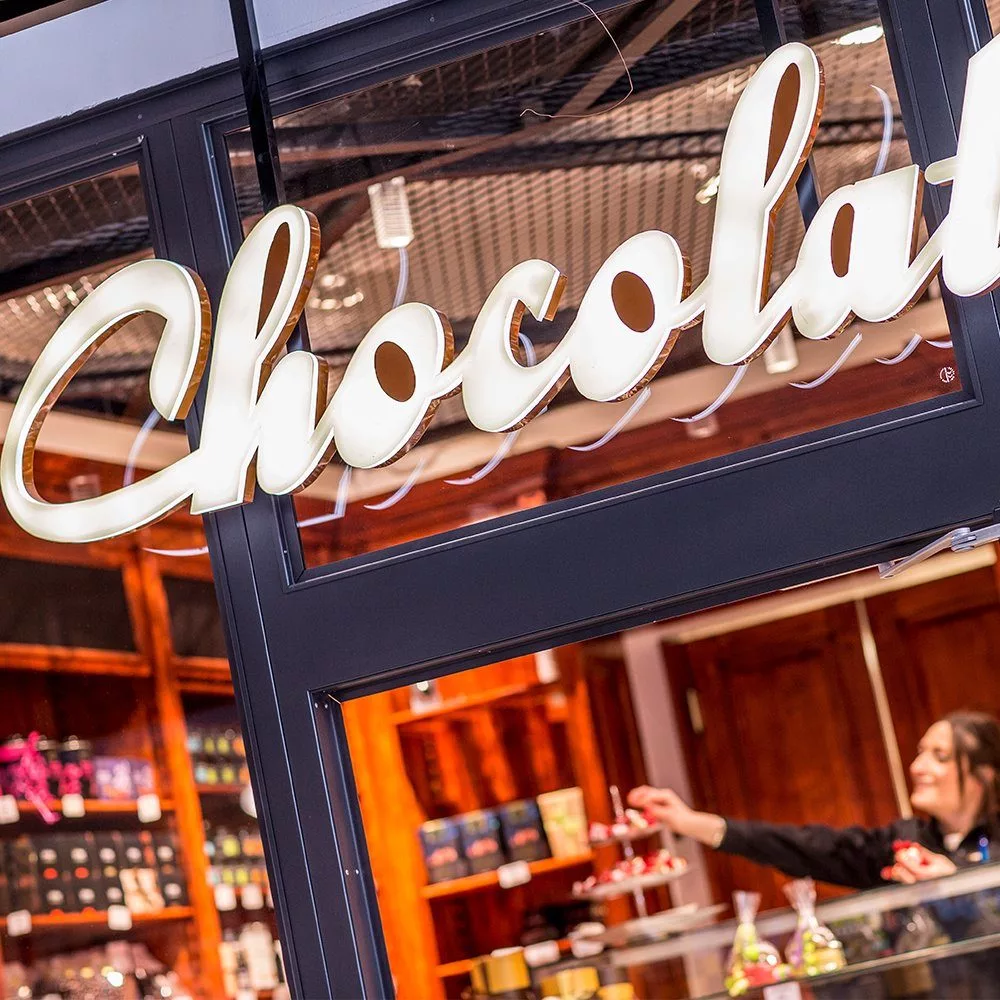 En skylt med texten "Chocolate" ovanför en butik med choklad och en person bakom disken.