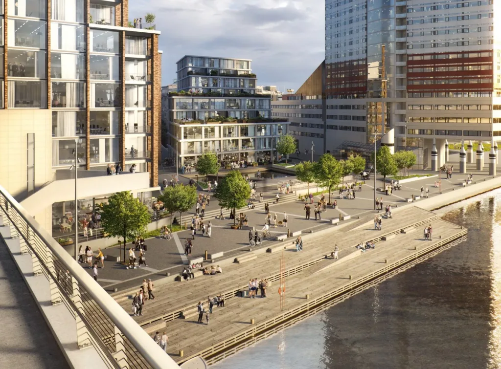 En stadsbild med moderna byggnader, människor som promenerar och sitter vid vattnet.