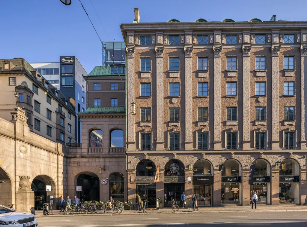 En byggnad med klassisk arkitektur och flera valv, omgiven av stadsliv och cyklar på gatan.