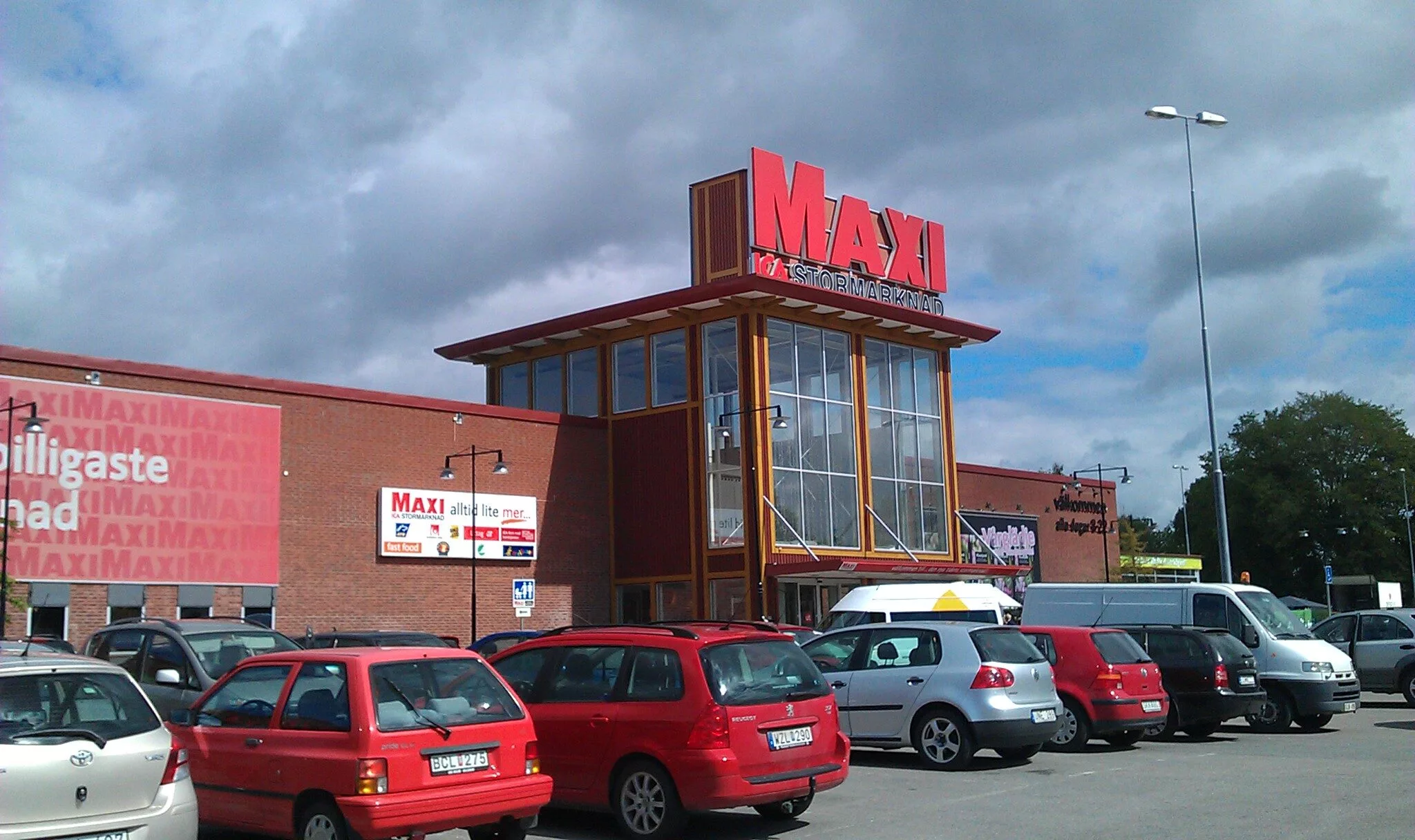 En stormarknadsbyggnad med röda bilar parkerade framför och skylten "MAXI ICA Stormarknad".