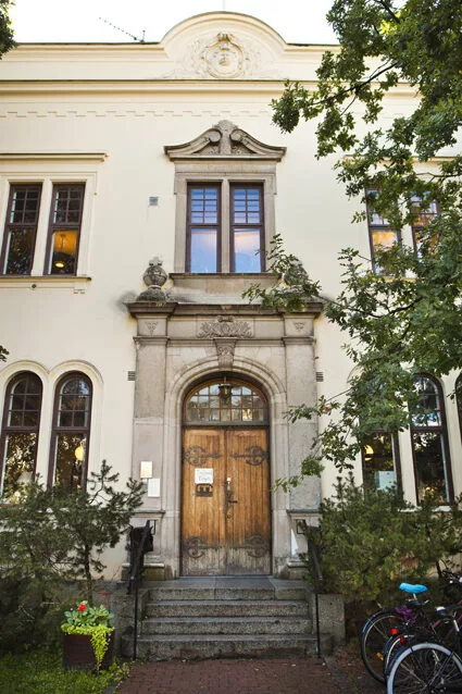 En äldre byggnad med detaljerad arkitektur, trädgrenar framför och en stor träport.