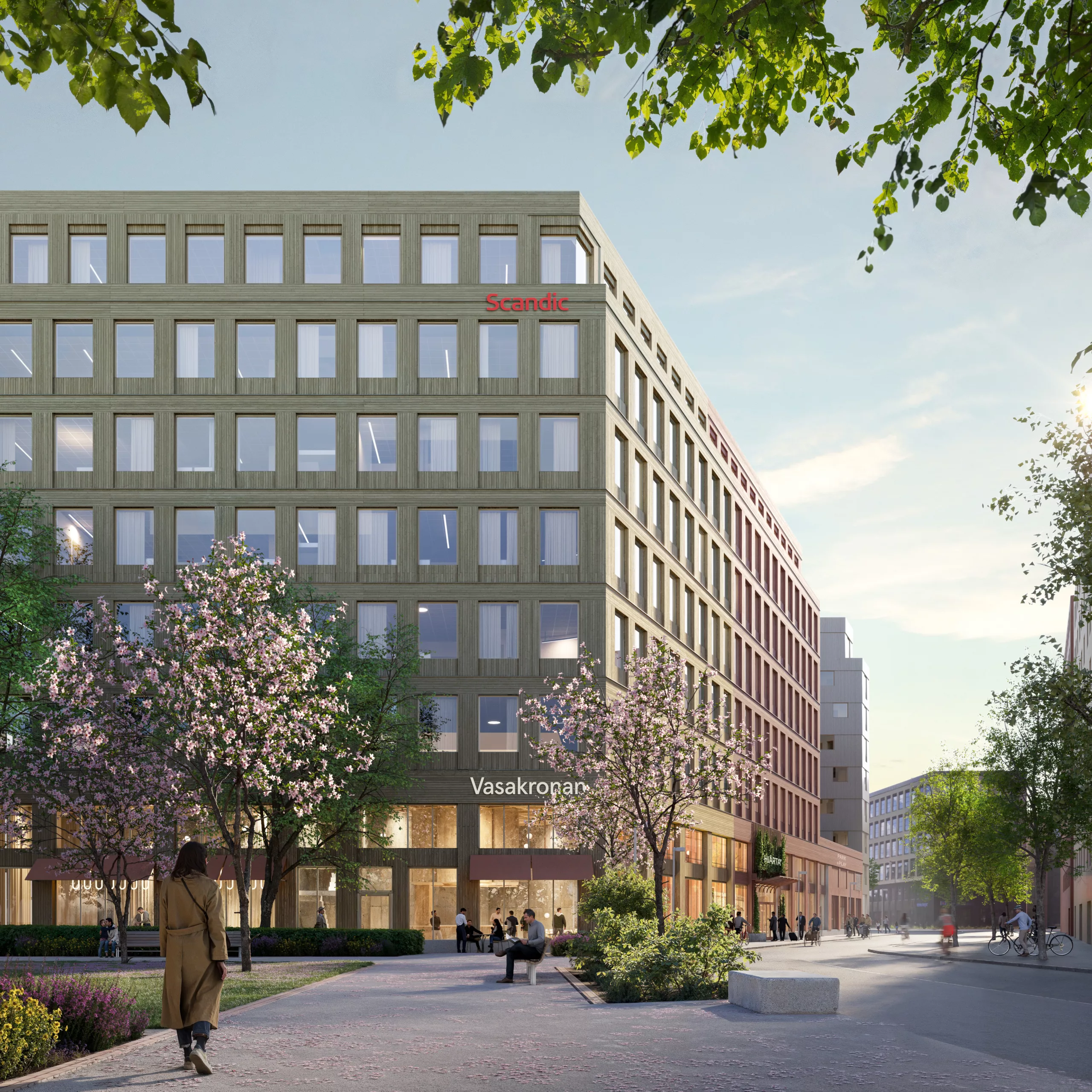 En modern byggnad med stora fönster omgiven av träd och gångvägar.