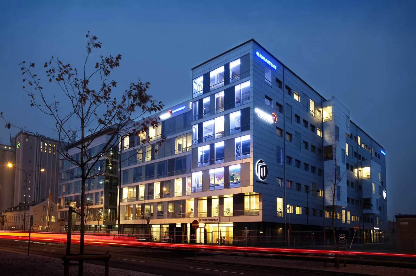 Ett modernt flerfamiljshus med lysande blå neonskyltar i skymningen.