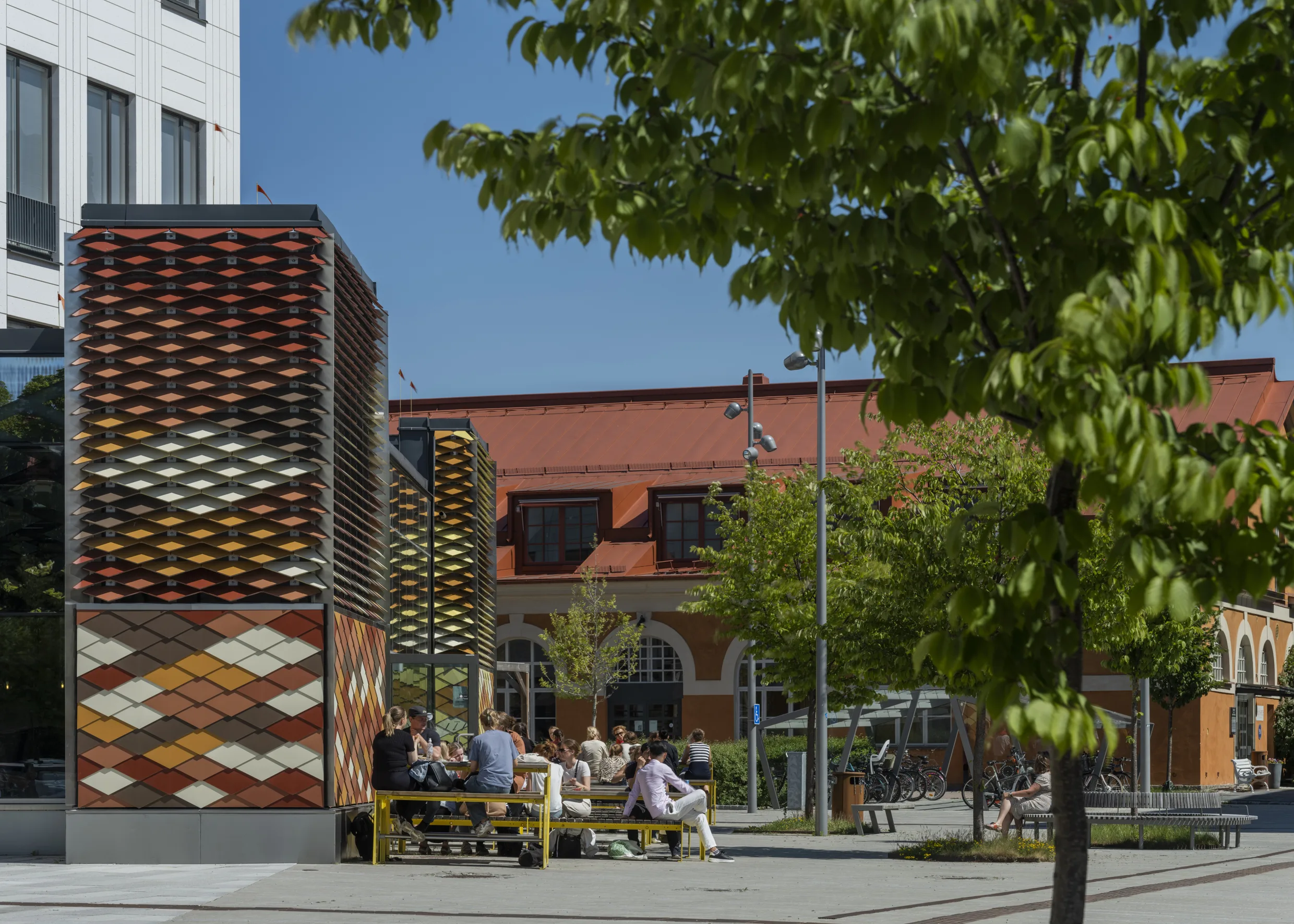 5. En utomhusmiljö med människor som sitter på bänkar, färgglada väggar och träd i närheten.