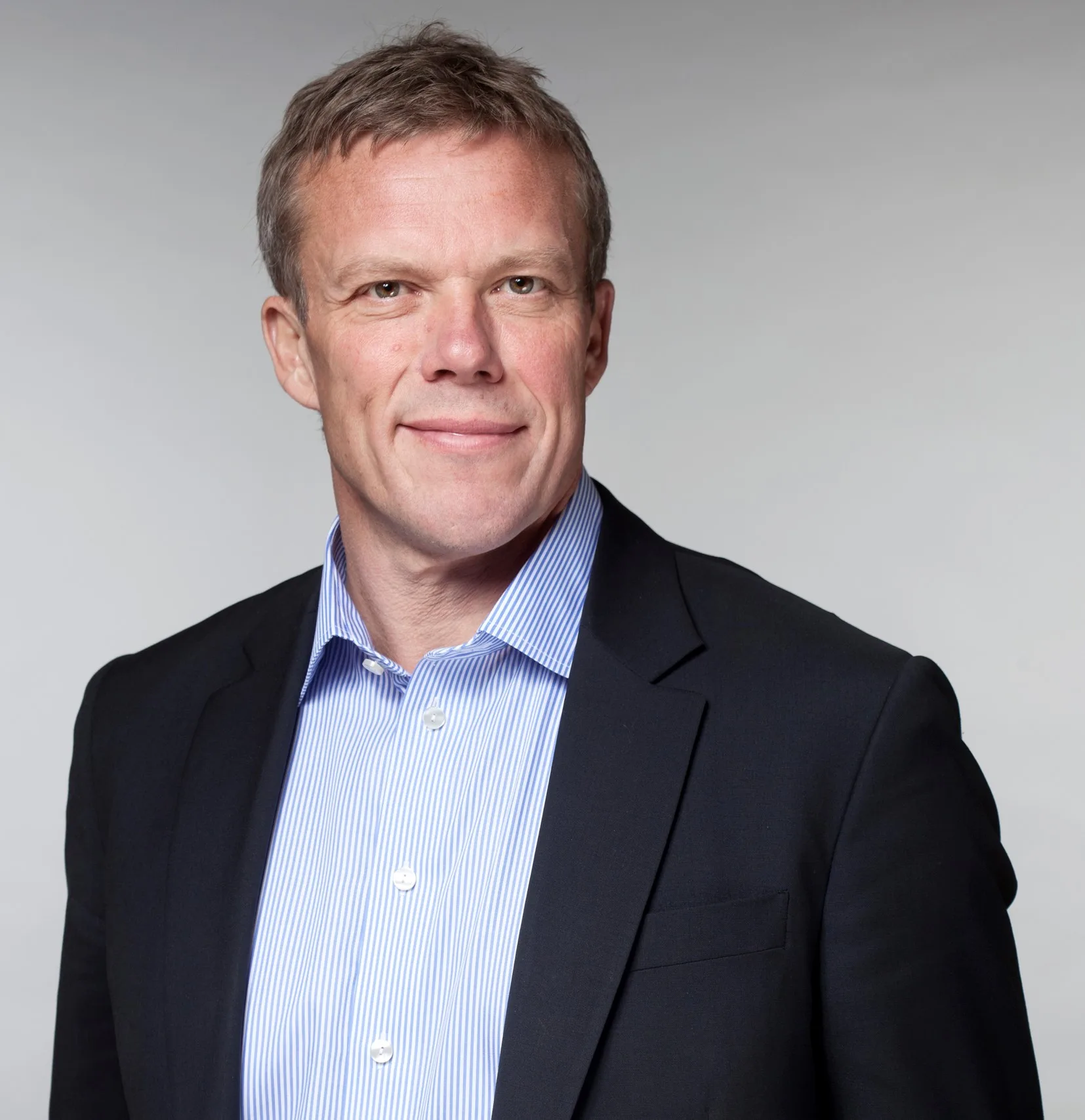 4. En man i kostym och blå skjorta står mot en ljusgrå bakgrund.