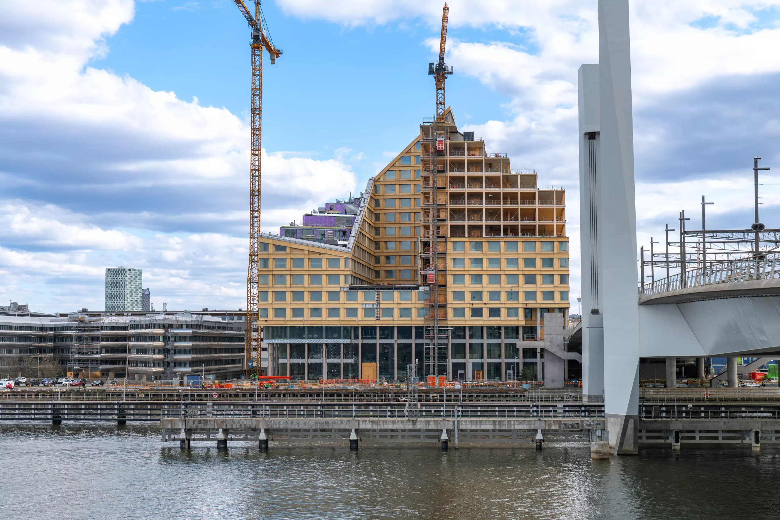 2. En byggnad under konstruktion med en unik trappstegsdesign, omgiven av lyftkranar vid vattnet.