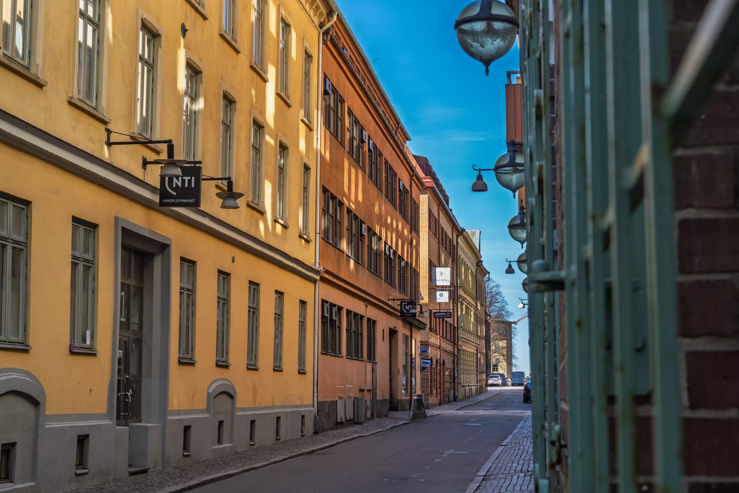 En smal kullerstensgata med färgglada byggnader och gatlampor under en klarblå himmel.