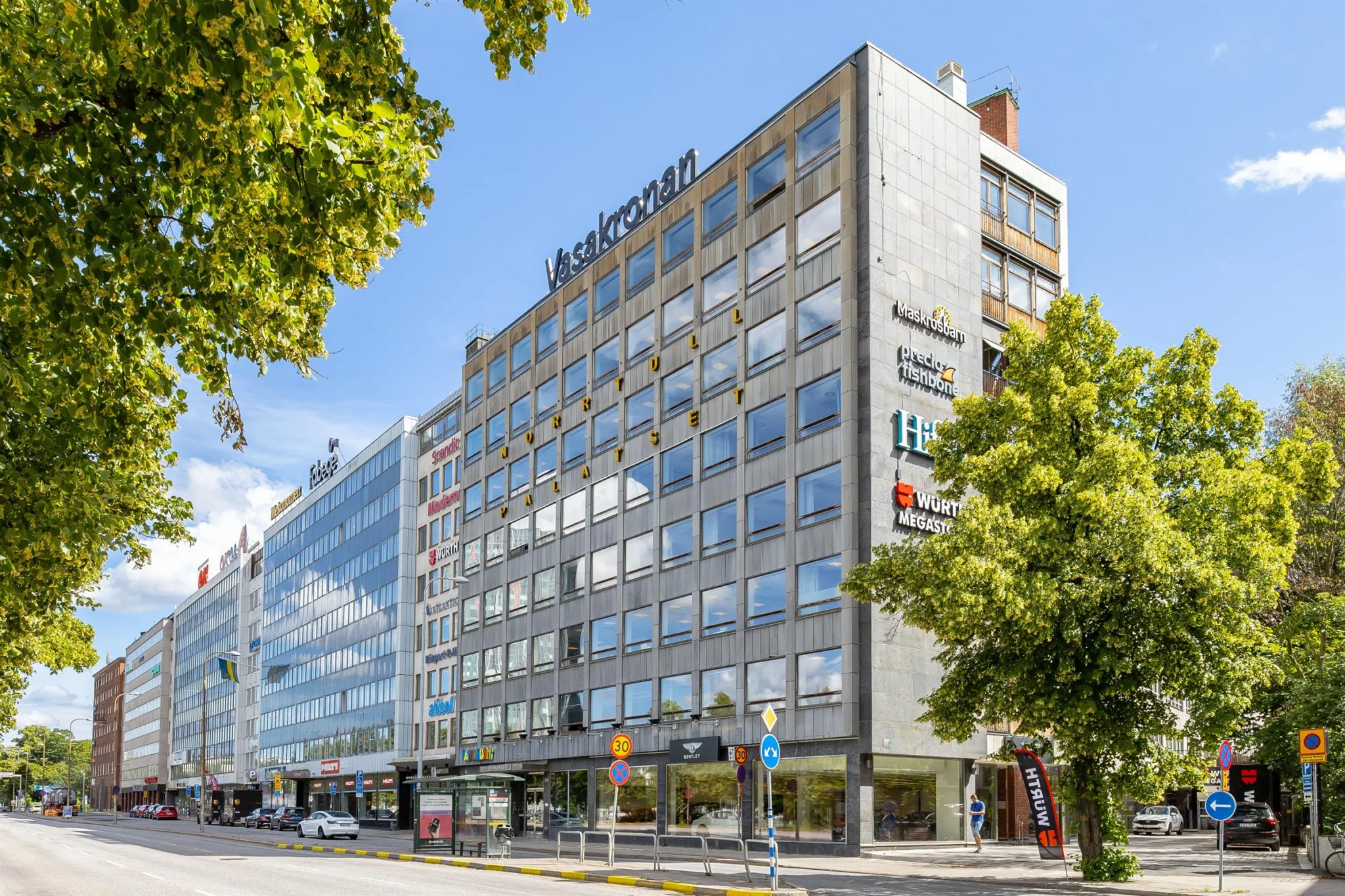 2. Modern kontorsbyggnad med flera våningar och skyltar för företag på fasaden.