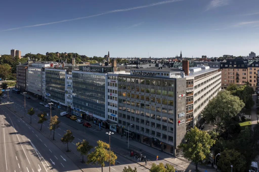 Exteriör av ett kontorshus med glasfasad och omgivande träd längs gatan.