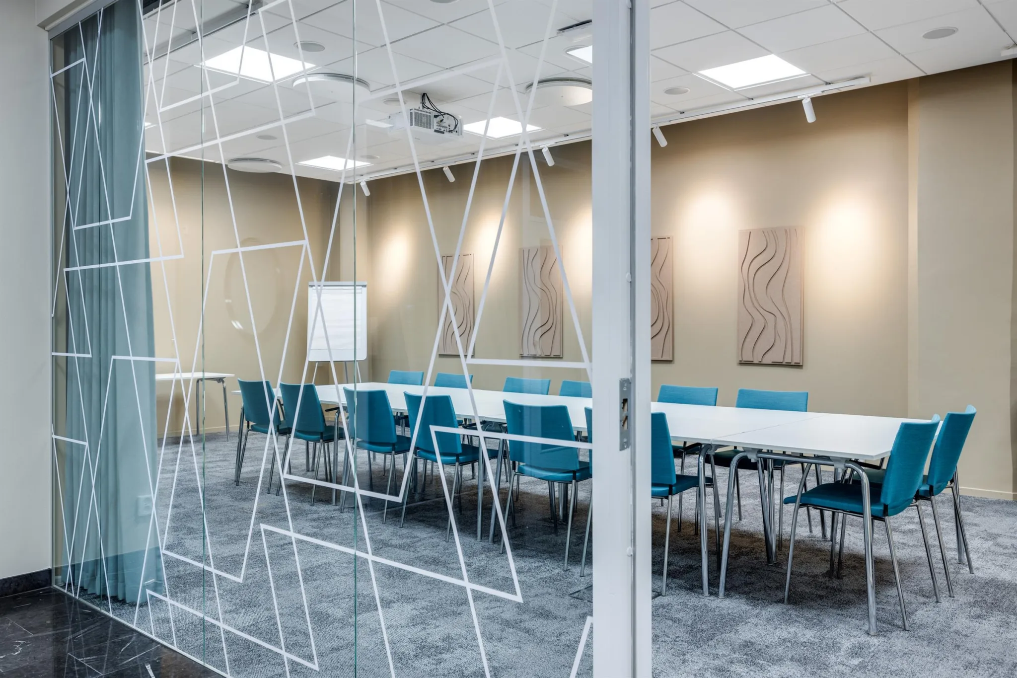 4. Ett konferensrum med blå stolar, vita bord och glasväggar med ett geometriskt mönster.