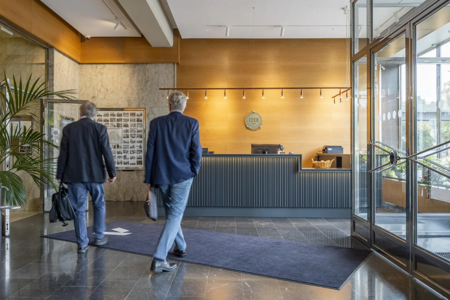 1. Två personer går mot en receptionsdisk i ett hotell med en modern och ljus inredning.