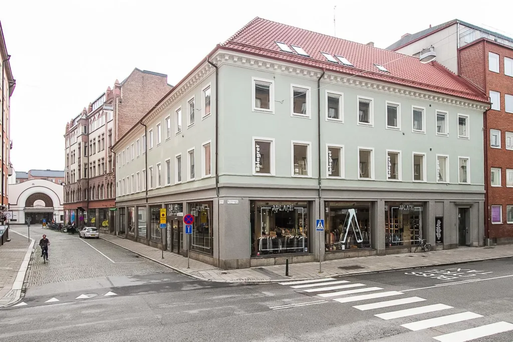 En ljusgrön byggnad med röda tak, stora skyltfönster och ett övergångsställe vid hörnet.
