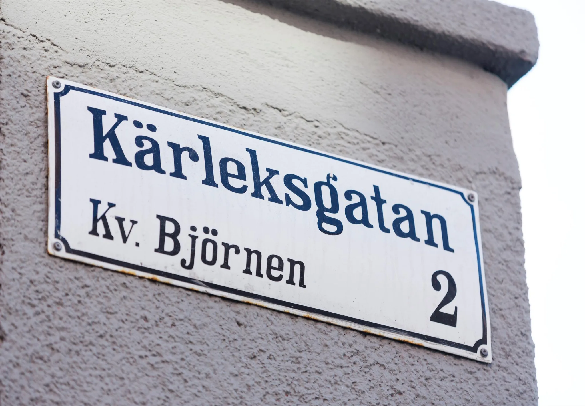 En vit gatunamnskylt på en grå vägg med texten "Kärleksgatan, Kv. Björnen, 2".