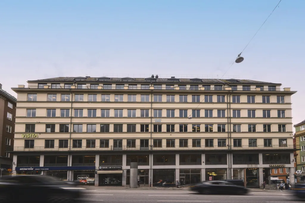 En gul byggnad med flera våningar och stora fönster, omgiven av en bred gata med bilar.