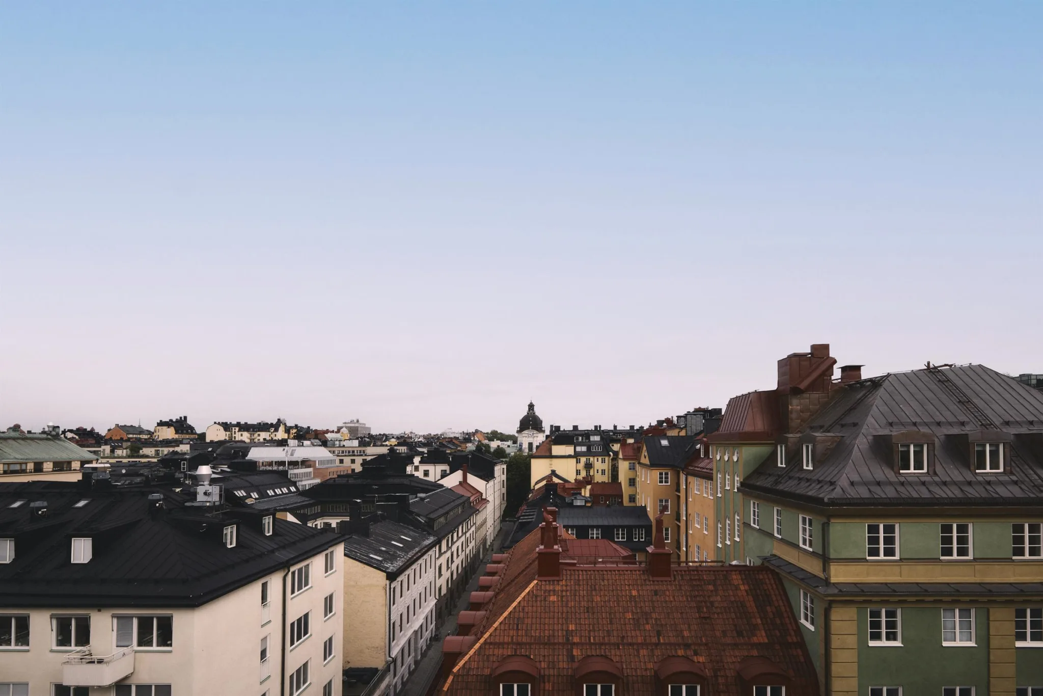 En vy över hustak i ett bostadsområde med mörka och röda tak, sett under en klar himmel.