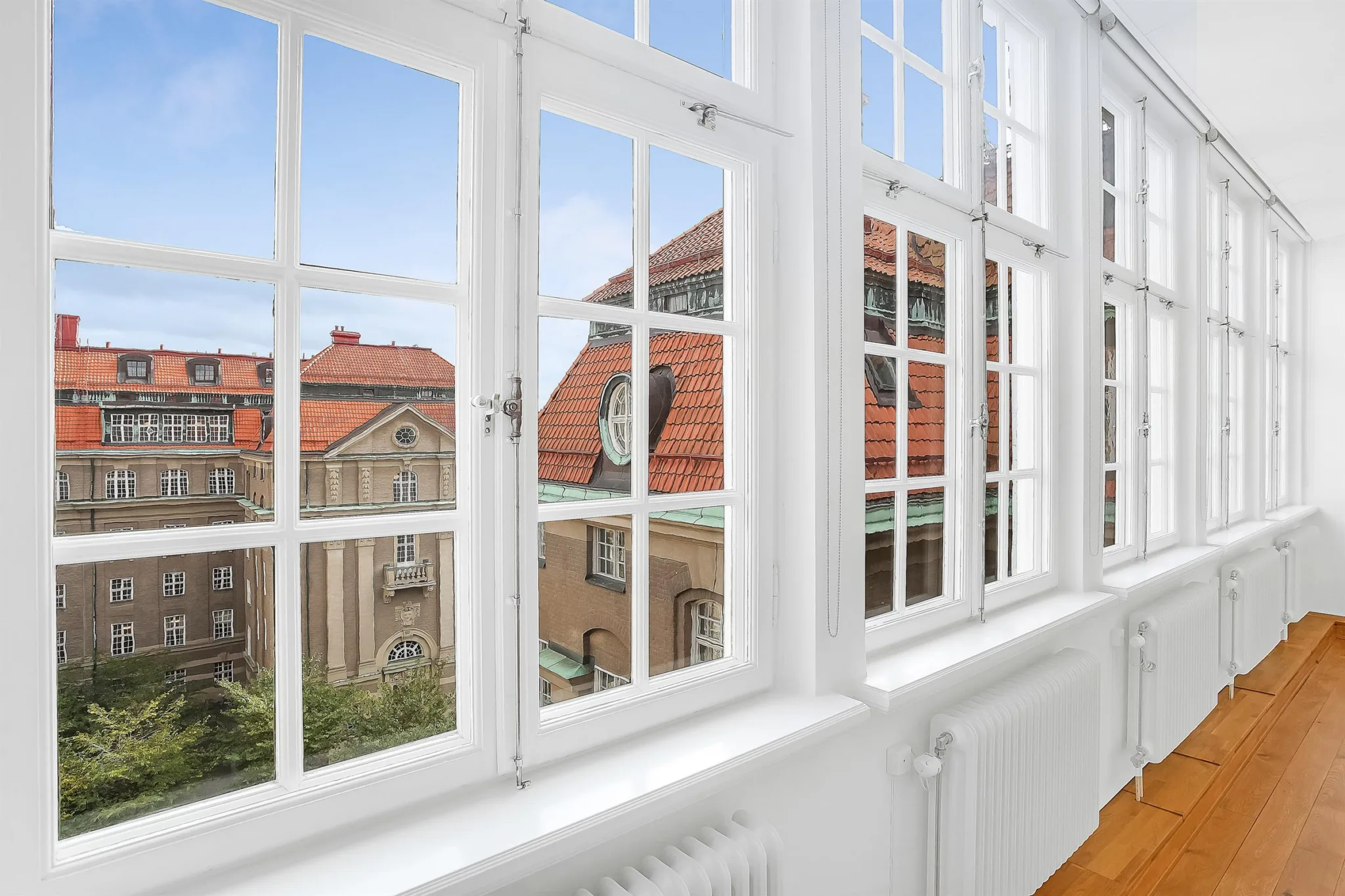 Ett stort fönster med vitramar som visar en utsikt över byggnader med röda tak.