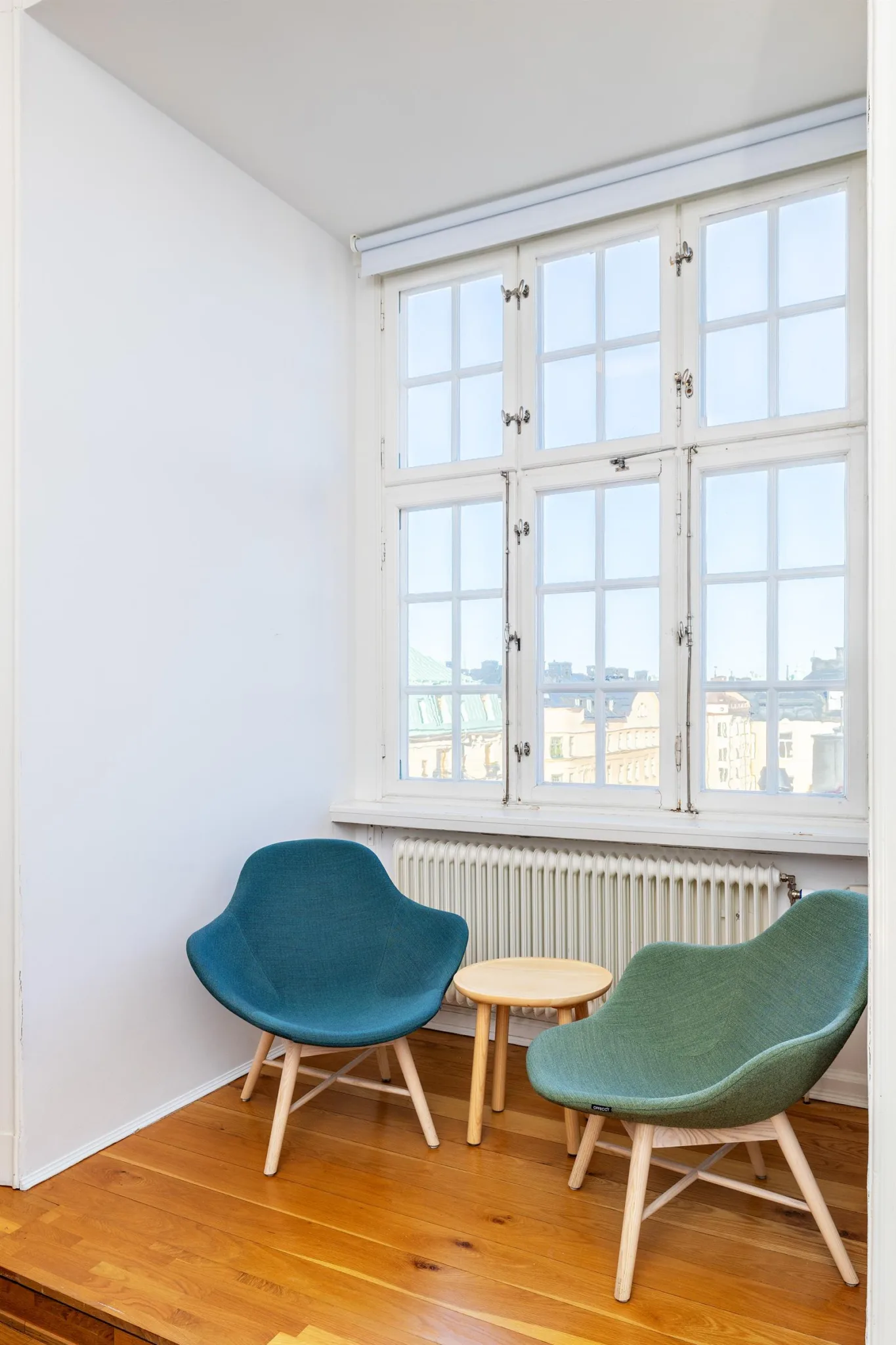 En sittgrupp med två färgglada stolar och ett litet bord framför ett stort fönster.