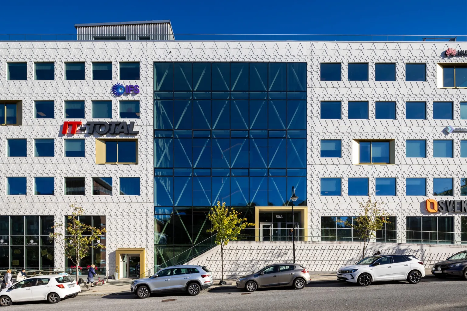 4. En modern byggnad med vit fasad och stora triangelformade glasfönster, parkerade bilar framför.