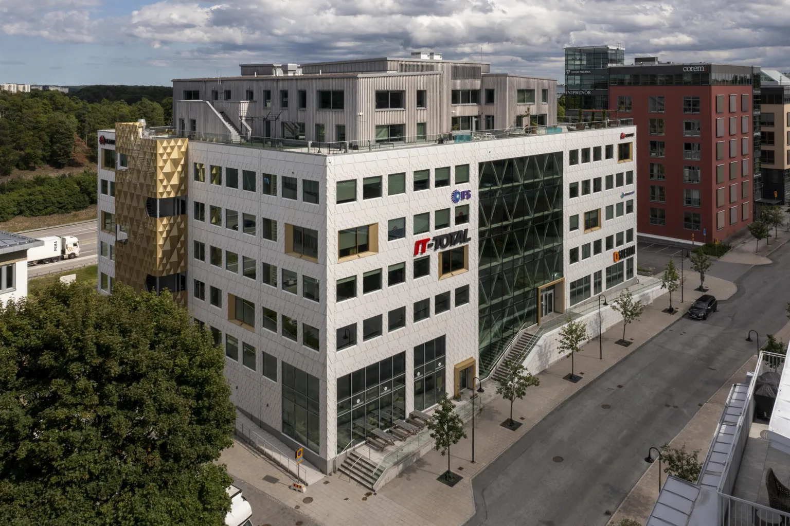 5. En vit kontorsbyggnad med stora fönster och flera våningsplan, omgiven av andra byggnader och en gata.