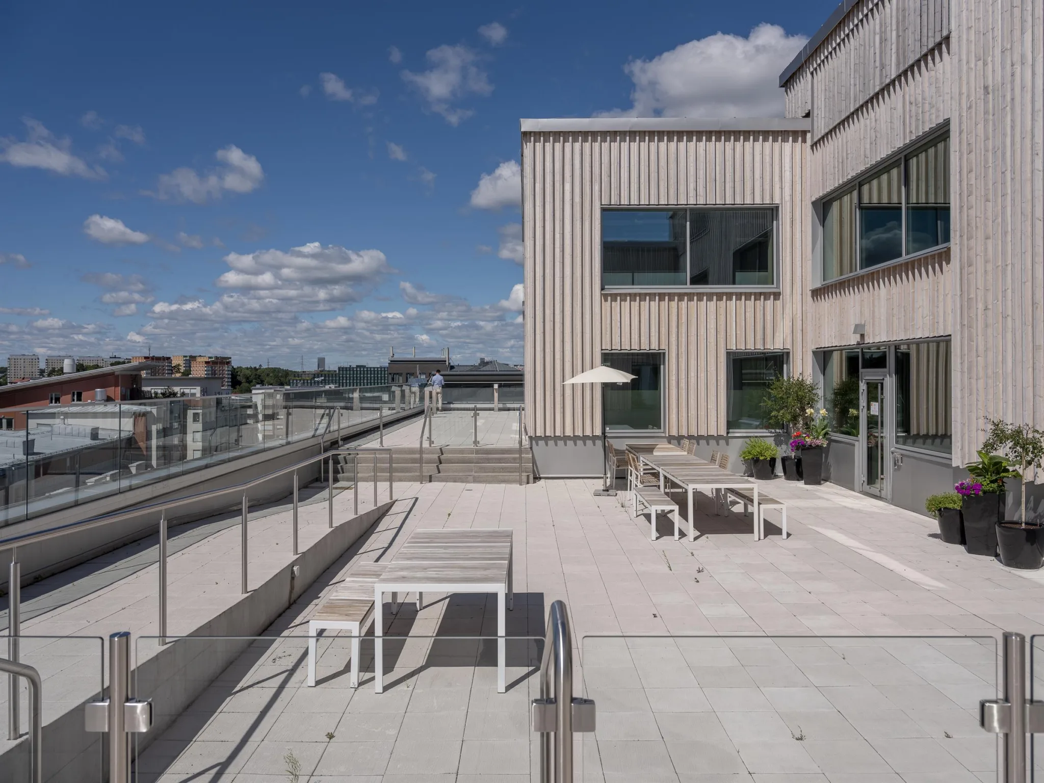 5. En takterrass med sittplatser, parasoll och utsikt över en stad under en klarblå himmel.